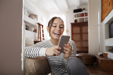 Happy woman text messaging while sitting at home - CAVF37288