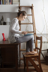 Frau liest ein Buch, während sie auf einem Holztisch zu Hause sitzt - CAVF37290