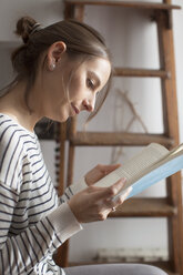 Nahaufnahme einer Frau, die zu Hause sitzt und ein Buch liest - CAVF37291