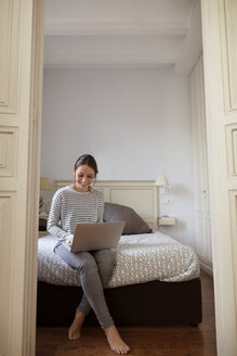 Frau benutzt Laptop, während sie zu Hause auf dem Bett sitzt - CAVF37292