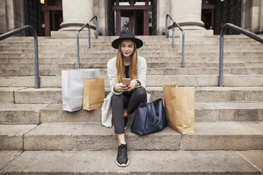 Woman text messaging while sitting by shopping bags on steps - CAVF37303