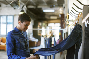 Ein lächelnder Modedesigner prüft in einer Werkstatt die auf einem Gestell hängenden Jeans - CAVF37317