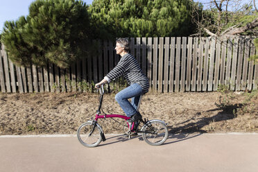 Side view of woman cycling on road by fence - CAVF37331