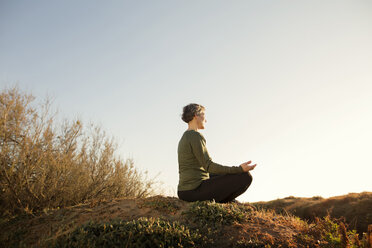 Woman meditating on top of rock against clear sky - CAVF37347