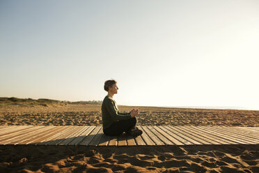 Side view of woman meditating on footpath at beach against clear sky - CAVF37350