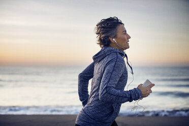 Frau beim Joggen und Musikhören am Strand gegen den Himmel - CAVF37360
