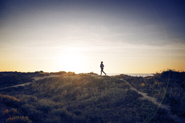 Entfernte Ansicht einer joggenden Frau auf einem Feld gegen den Himmel - CAVF37373