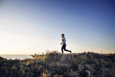 Frau in voller Länge beim Joggen auf einem Feld gegen den klaren Himmel - CAVF37375