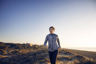 Front view of woman jogging at beach against clear sky - CAVF37376