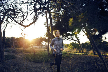 Woman jogging on field by trees during sunrise - CAVF37377