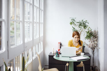 Businesswoman using phone while sitting at table with laptop in office - CAVF37400