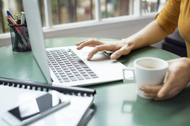 Abgeschnittenes Bild einer Geschäftsfrau, die eine Kaffeetasse hält und einen Laptop im Büro benutzt - CAVF37402