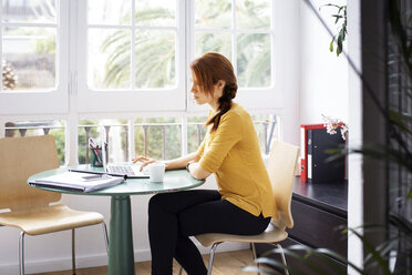 Geschäftsfrau sitzt auf einem Stuhl und arbeitet an einem Laptop in einem kreativen Büro - CAVF37403