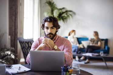 Porträt eines Geschäftsmannes, der am Tisch mit Laptop in einem kreativen Büro sitzt - CAVF37429