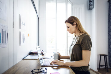 Seitenansicht einer Geschäftsfrau mit Laptop am Schreibtisch in einem kreativen Büro - CAVF37434