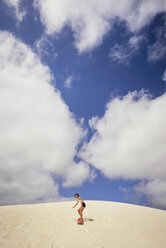 Girl sandboarding in desert against cloudy sky - CAVF37479