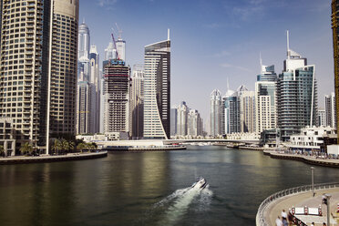 Boot fährt auf dem Dubai Creek inmitten moderner Gebäude gegen den Himmel - CAVF37499