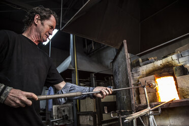 Glasbläser erhitzen geschmolzenes Glas am Ofen in der Werkstatt - CAVF37548