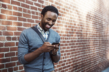 Man text messaging while standing against brick wall - CAVF37552