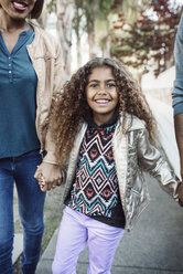 Porträt eines glücklichen Mädchens, das mit seinen Eltern auf dem Gehweg spazieren geht - CAVF37553