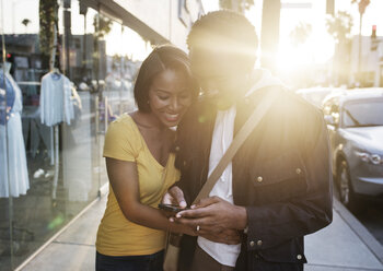 Woman embracing man using phone while standing on sidewalk - CAVF37567