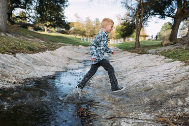 Full length of boy jumping over stream at park - CAVF37591