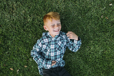 Overhead view of happy boy lying on grassy field at park - CAVF37593