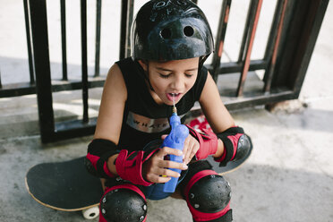 Hohe Winkel Ansicht der müde Mädchen trinken Wasser, während auf Skateboard sitzen - CAVF37605