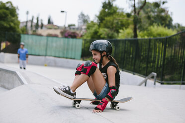 Seitenansicht eines verspielten Mädchens, das auf einem Skateboard auf einer Sportrampe sitzt - CAVF37607