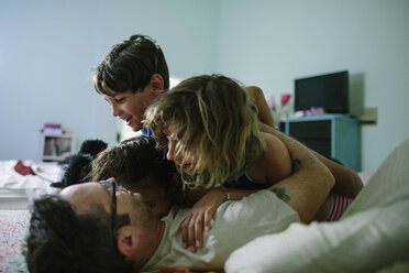 Happy siblings embracing father on bed at home - CAVF37610