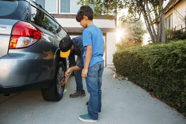 Sohn sieht Vater beim Festziehen von Reifen mit Schraubenschlüssel in der Einfahrt an - CAVF37612