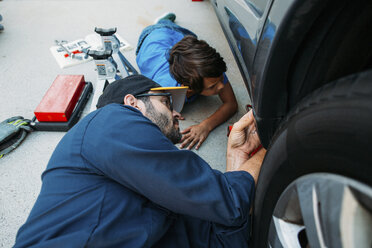 Hoher Blickwinkel des ernsten Vaters, der seinem Sohn beibringt, ein Auto in der Einfahrt zu reparieren - CAVF37615