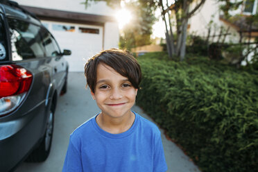 Porträt eines glücklichen Jungen, der in einer Einfahrt neben einem Auto steht - CAVF37617