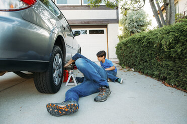 Father teaching son to repair car while lying down at driveway - CAVF37619