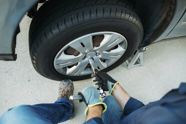 High angle view of man tightening tire with spanner at driveway - CAVF37622