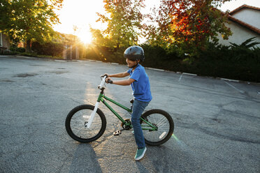 Junge mit Fahrradhelm beim Fahrradfahren bei Sonnenuntergang - CAVF37623