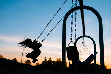 Silhouette girl swinging at playground against sky during dusk - CAVF37626