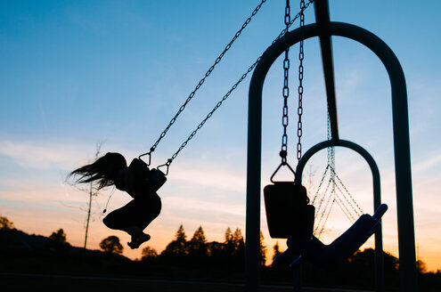 Silhouette Mädchen schaukeln auf dem Spielplatz gegen den Himmel in der Abenddämmerung - CAVF37626