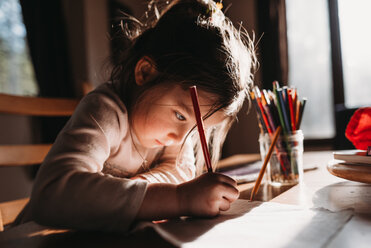 Girl drawing with colored pencil on paper while sitting at table - CAVF37636