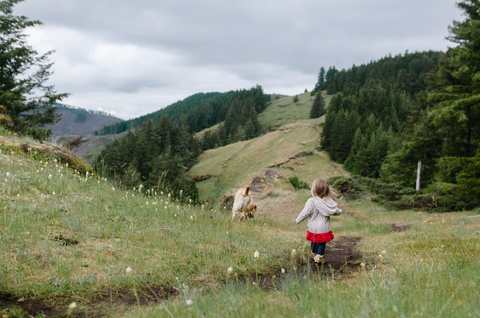 Rückansicht eines Mädchens, das mit seinem Hund auf einer Wiese spazieren geht, vor einem Hügel, lizenzfreies Stockfoto