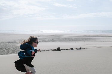 Seitenansicht eines Mädchens mit ausgestreckten Armen, das am Strand gegen den Himmel läuft - CAVF37641