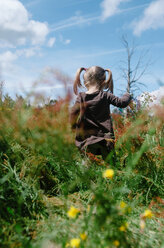 Low angle view of girl standing on field against cloudy sky during sunny day - CAVF37642