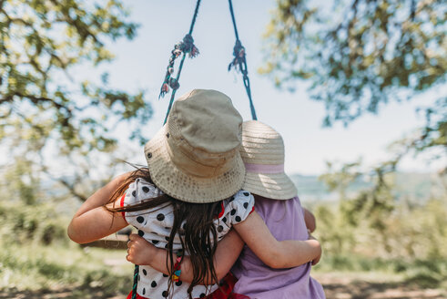 Rear view of sisters wearing hats sitting on rope swing - CAVF37646