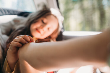 Mädchen spielt im Auto sitzend mit Inchworm auf dem Knie - CAVF37648