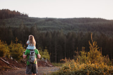 Rückansicht eines Vaters, der seine Tochter auf den Schultern trägt, während er auf einem Feld steht - CAVF37653