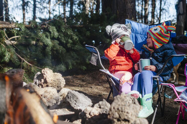 Glückliche Schwestern, die auf einem Campingplatz im Wald sitzen und etwas trinken - CAVF37662