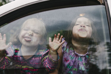 Playful sisters making faces while traveling in car seen through window - CAVF37663
