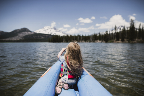 Rückansicht eines Mädchens, das auf einem Schlauchboot auf einem See sitzt, lizenzfreies Stockfoto