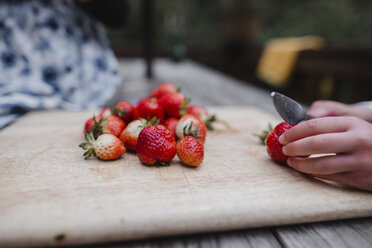 Cropped hands of girl cutting strawberry on cutting board at table - CAVF37675