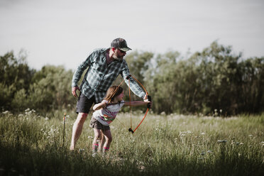 Vater hilft Tochter bei der Verwendung von Pfeil und Bogen auf einer Wiese - CAVF37691